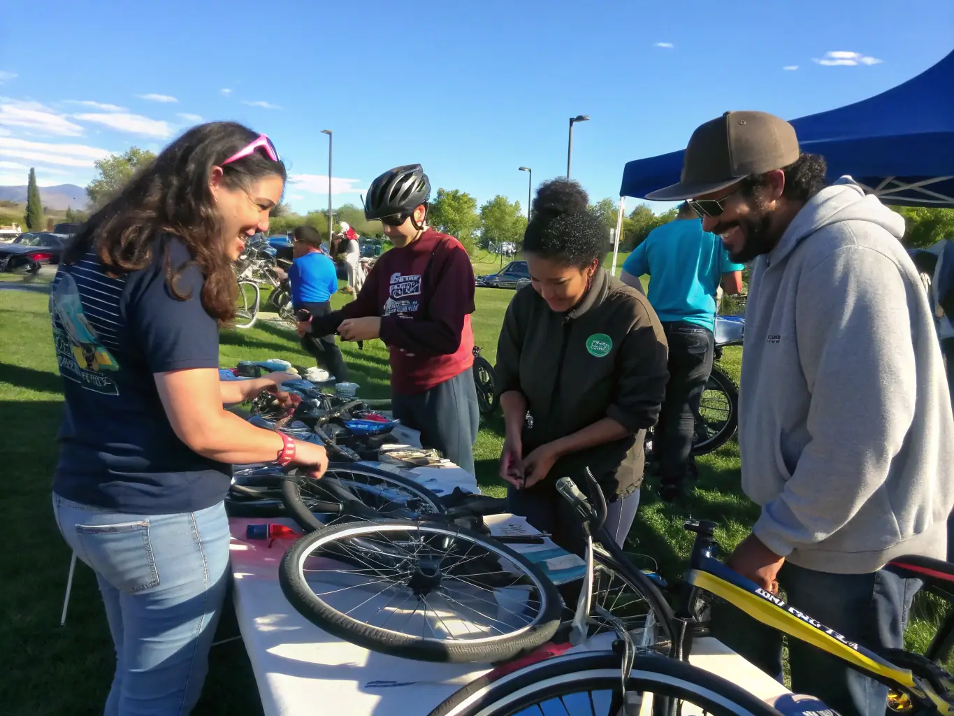 A group of volunteers working together to maintain bicycles in a workshop setting. The scene is well-lit and organized, with various tools and spare parts visible. The volunteers are smiling and engaged in their tasks.